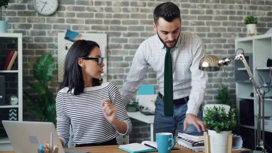 Two colleagues discussing documents beside a laptop